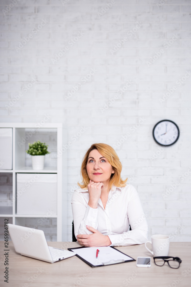 cheerful mature business woman sitting in office and dreaming about something - copy space over white wall cheerful mature business woman sitting in office and dreaming about something - copy space over white wall