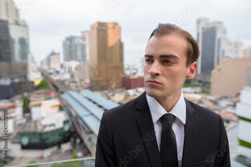 Young businessman thinking outdoors in city with rooftop view