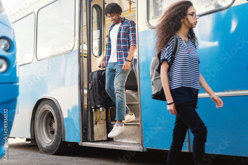 Young African American man getting off the bus with luggage in his hand.