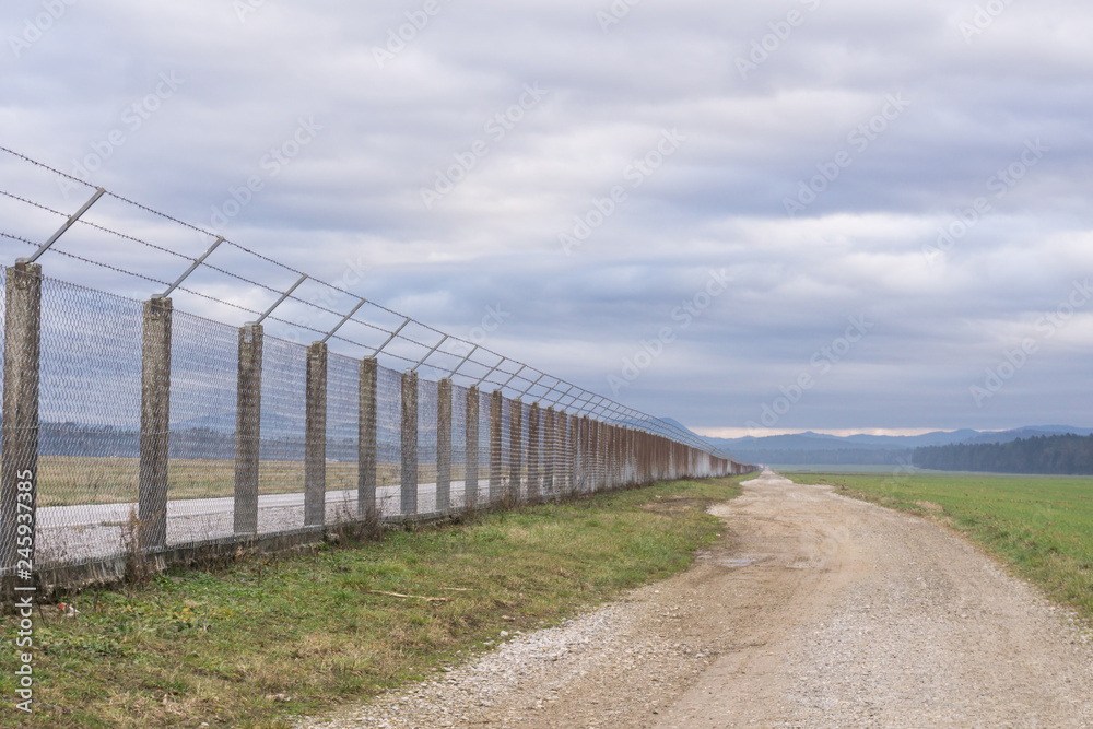 Long country road stretching off past a lone tree to the distant horizon with fence on the right Long country road stretching off past a lone tree to the distant horizon with fence on the right