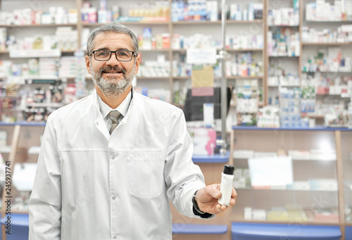 Pharmacist in white coat smiling, posing in drugstore.