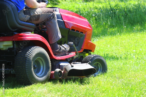 Obraz na plátně Gardener driving a riding lawn mower in a garden