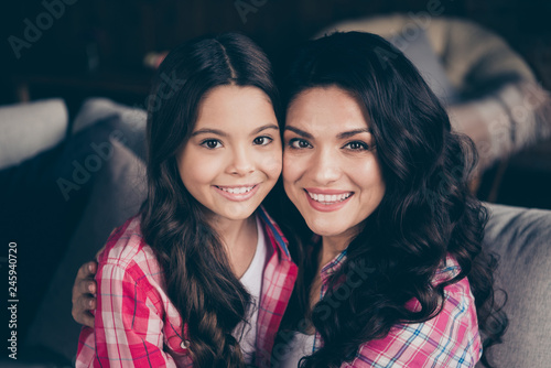 Close up photo two people mum little daughter glad weekend communicate holding hands arms look similar leisure rejoice wear pink plaid shirts jeans bright flat apartment room sit on cozy sofa