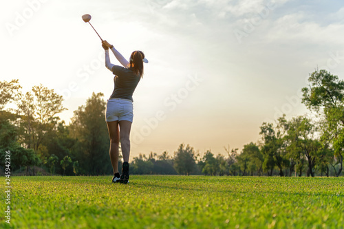 Sport Healthy. Asian sporty woman golf player doing golf swing tee off on the green sunset evening time, she presumably does exercise. Healthy and Lifestyle Concept.