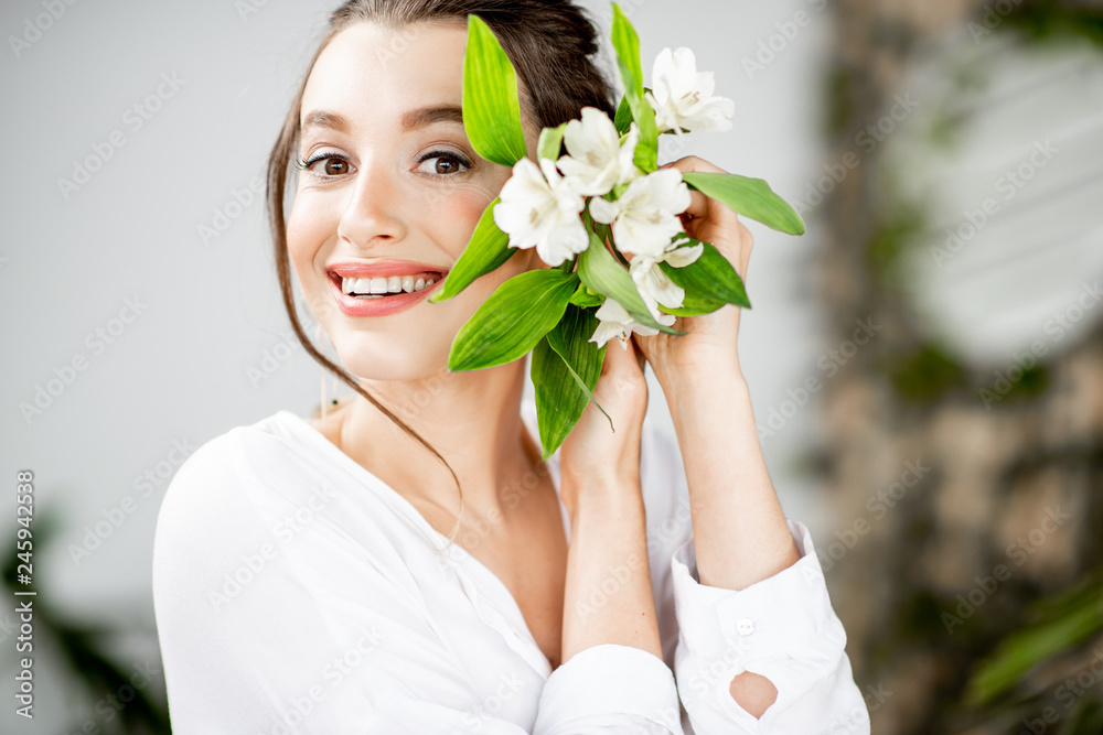 Close-up portrait of a beautiful woman in white shirt holding flower on her face indoors