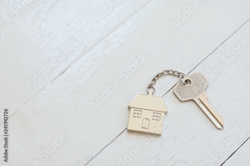 Home key with house keyring on white wood table background, property concept