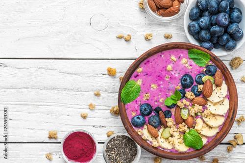 Smoothie bowl with fresh berries, nuts, seeds, granola and mint for healthy vegan diet breakfast on white wooden table