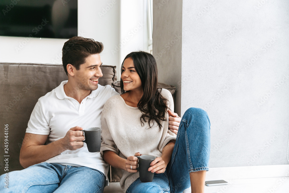 Happy lovely young couple holding cups while sitting on a floor Happy lovely young couple holding cups while sitting on a floor