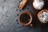 Cup with hot coffee, muffins and cinnamon sticks on the dark, textured background, top view