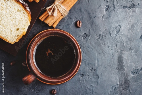 Cup with hot coffee, muffins and cinnamon sticks on the dark, textured background, top view