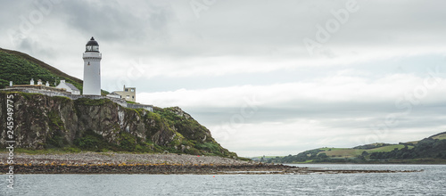 Irish shoreline panorama with Campbeltown lighthouse. Northern Ireland. Stunning English landscape. White lighthouse on the steep cliff. The shore panoramic view under the rainy cloudy sky. photo