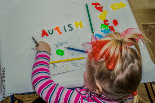 child draws with pencils. on the sheet is written the word AUTISM