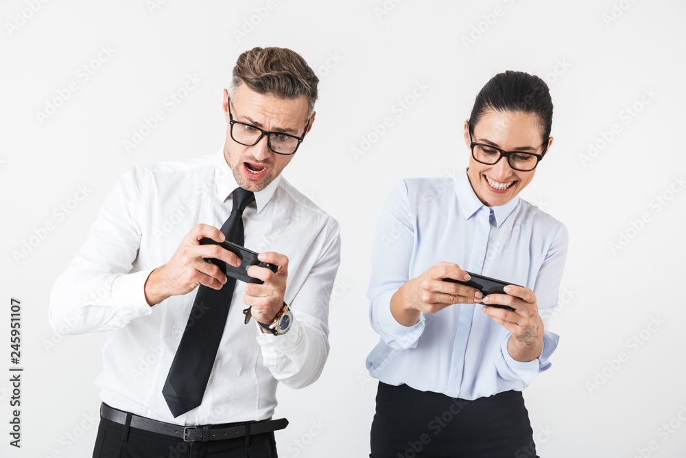 Emotional business colleagues couple isolated over white wall background play games by mobile phones. Emotional business colleagues couple isolated over white wall background play games by mobile phones.
