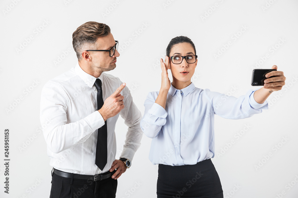 Young business colleagues couple isolated over white wall background take selfie by mobile phones. Young business colleagues couple isolated over white wall background take selfie by mobile phones.
