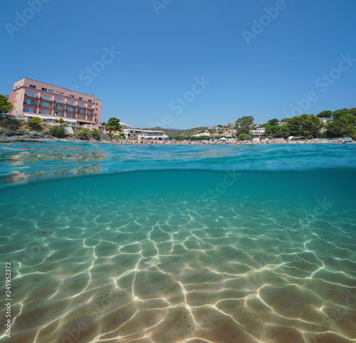 Spain beach with an hotel in Llanca on the Costa Brava and a sandy seabed underwater, split view half over and under water, Mediterranean sea, Platja de Grifeu, Catalonia