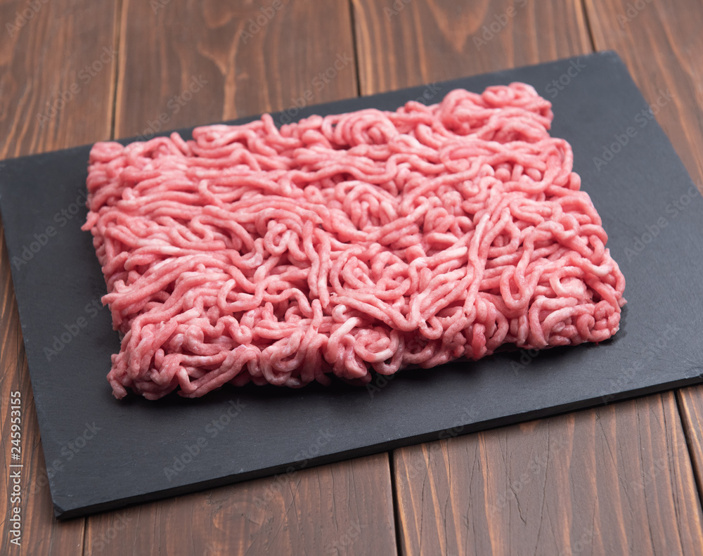Fresh minced pork on black plate and wooden background.
