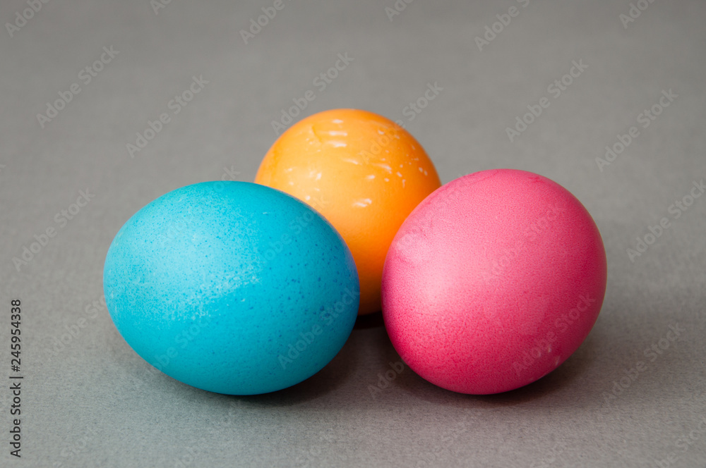 Three easter eggs blue pink orange color on a gray background. View from the side.