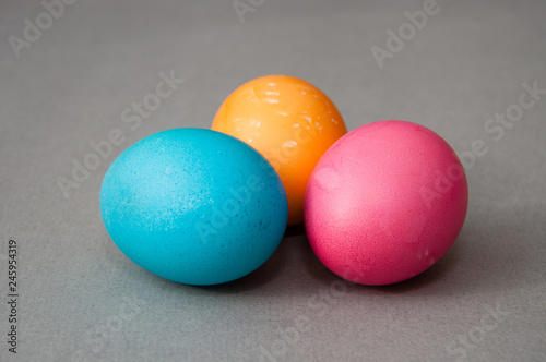 Three easter eggs blue pink orange color on a gray background. View from the side.