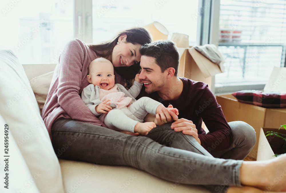 A portrait of young couple with a baby and cardboard boxes moving in a new home. A portrait of young couple with a baby and cardboard boxes moving in a new home.