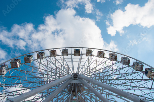 Ferris wheel in an amusement park, view from below look upwards. Sky background with clouds with place for text.