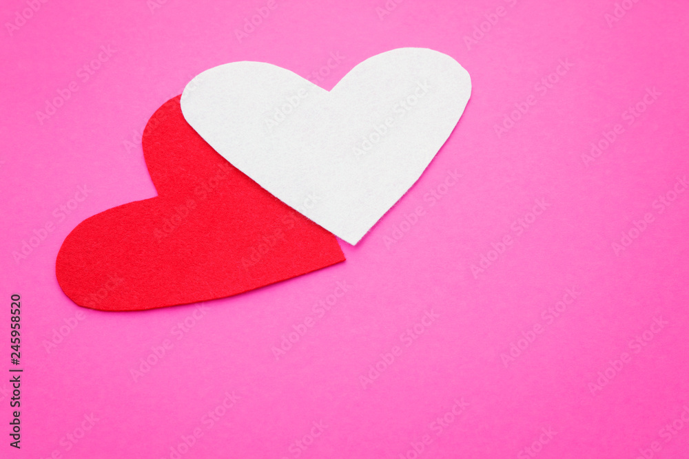 Two felt form of hearts on a pink background