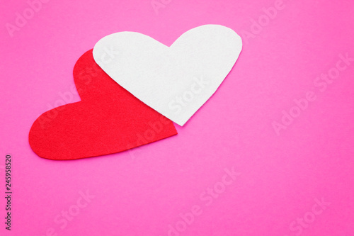 Two felt form of hearts on a pink background