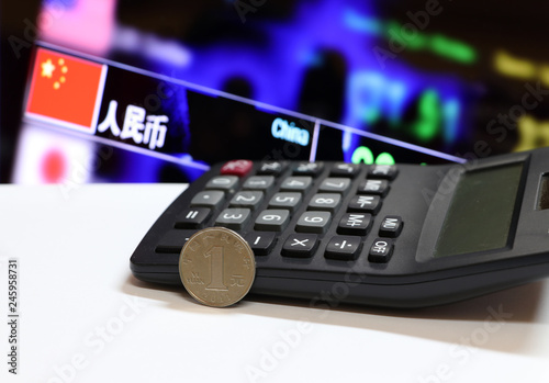 Chinese one Yuan coins on reverse (CNY) Bank name ZHONGHUA RENMIN YINHANG in Chinese on white floor and calculator with digital board. photo