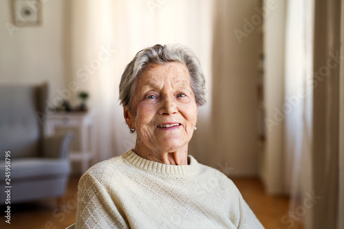 Quadro su tela A portrait of a senior woman sitting at home, looking at camera.