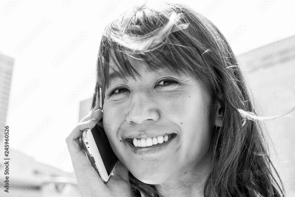 Happy Japanese woman smiling using a smartphone and looking at the camera Happy Japanese woman smiling using a smartphone and looking at the camera