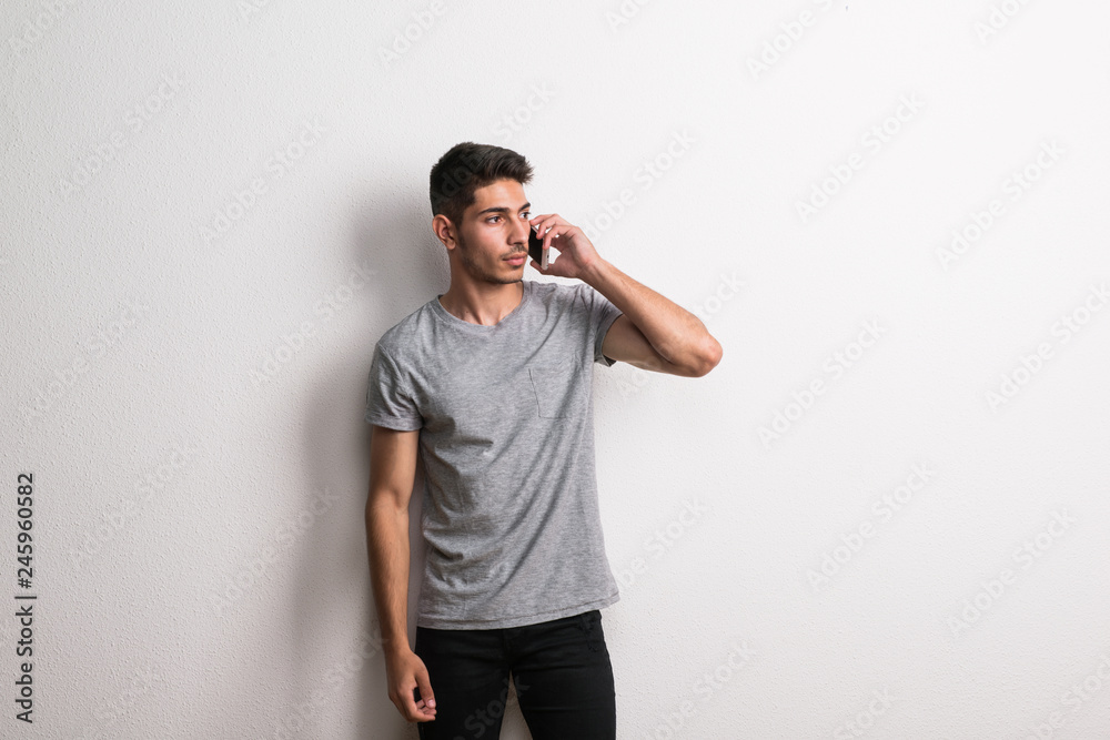 A cheerful young hispanic man with smartphone standing in a studio. A cheerful young hispanic man with smartphone standing in a studio.