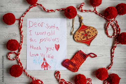 Overhead view of a child's letter to Santa Claus asking for superpowers on a table with a Christmas decoration photo