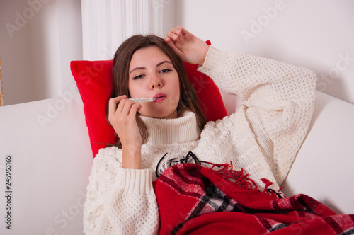 Sick woman lying on a bed with a thermometer. The girl measures the temperature. Severe headache, runny nose, migraine, flu, chills and fever. Concept medetsina and health