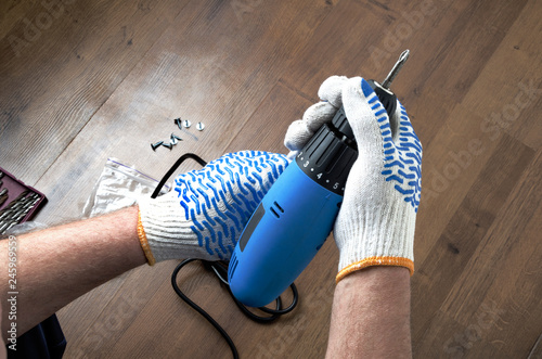 Top view of male hands using electric skrewdriver against wooden floor.Process of repair photo