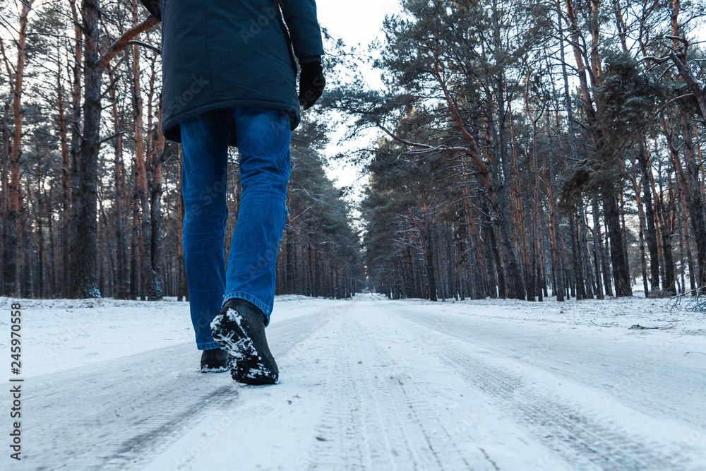 Men's legs in boots close up the snow-covered path in the winter forest, rear view Men's legs in boots close up the snow-covered path in the winter forest, rear view