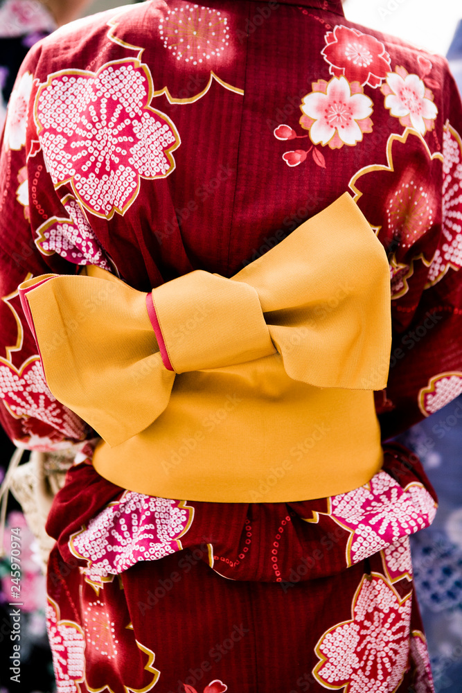 Detail of woman wearing red/maroon flower patterned summer kimono "yukata"  with bright orange “obi” belt. Stock Photo | Adobe Stock