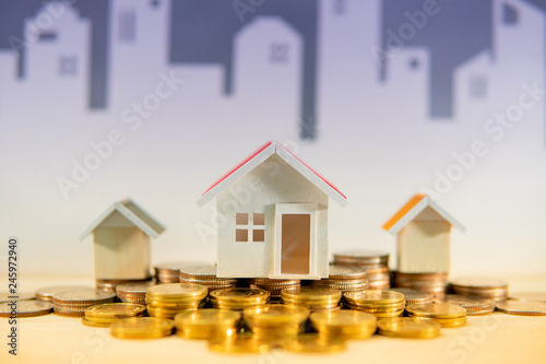 Real estate or property investment concept. Home mortgage loan rate. Gold coins stack and house models on the table with white city skyline background. Saving money for future retirement.