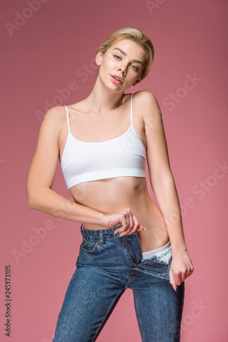 beautiful blonde woman posing in jeans and white bra, isolated on pink