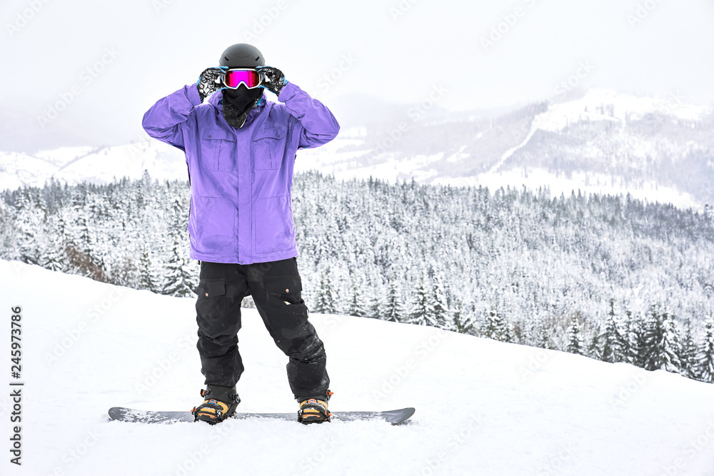 Snowboarder standing on his snowboard and straightening googles looking in  front of him with amazing mountain and wood view behind his back Stock  Photo | Adobe Stock