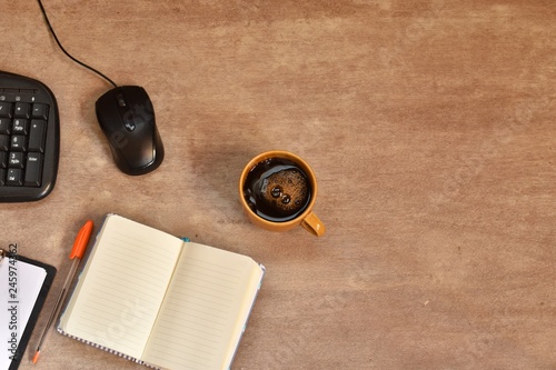 Workspace with blank note book, keyboard, and coffee cup on wooden background. 
