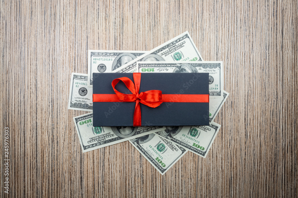 Black gift box with a bow with dollars banknotes on a wooden table. top view