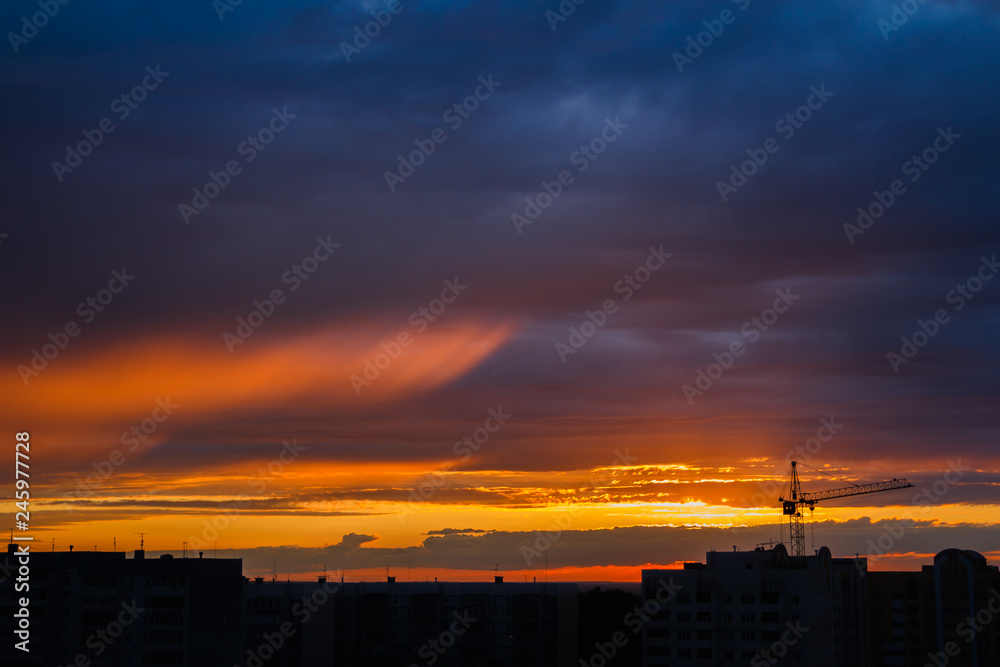 silhouette of construction crane and buildings against horizon of sunset sky