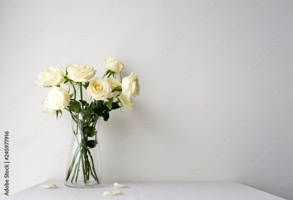 White roses in a glass vase on white table top on white background with copy space for product mockup placement for valentine's day wedding ceremony
