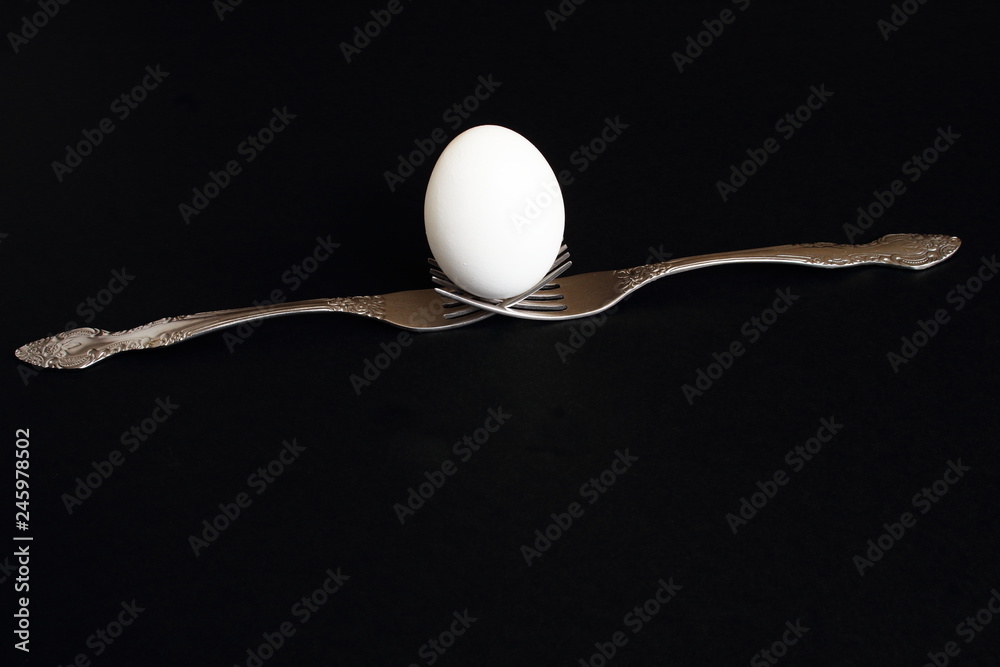 White egg on two silver forks on black background. Minimal background with copy space. White egg on two silver forks on black background. Minimal background with copy space.