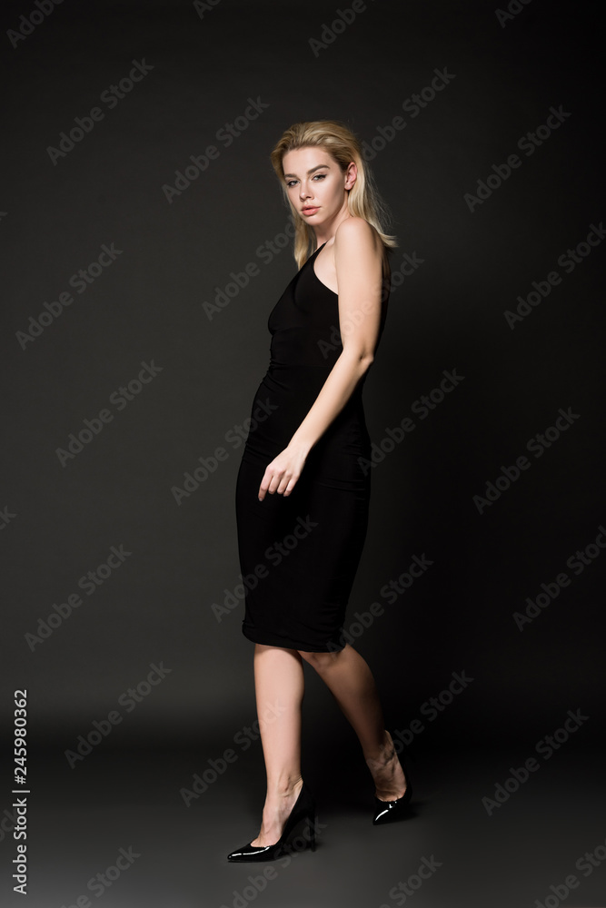 beautiful young woman in elegant black dress posing on black