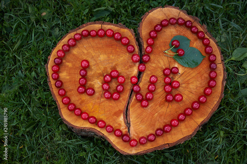 The heart and the word "love" are laid out with cherries on a cut wooden stump with a crack. Happy Valentine's Day. love concept. Summer sends love. Particles of art.