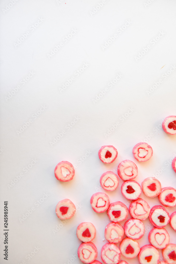 round red candy with a heart pattern lie on a white paper background as a texture and a corner frame