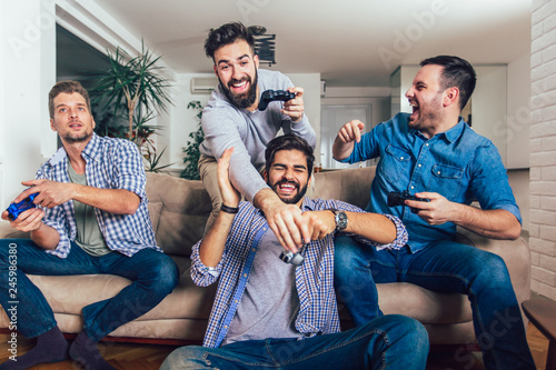 Smiling male friends playing video games at home and having fun. photo