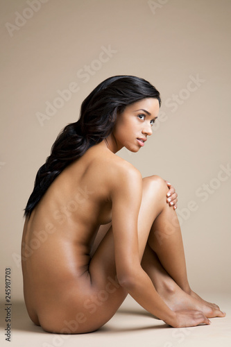 Naked young woman with black hair sitting indoors