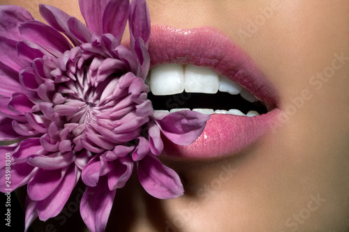 Close up of woman's lips with purple flower between her teeth