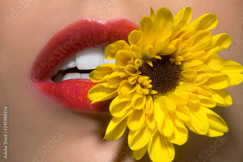Close up of woman's lips with yellow flower between her teeth